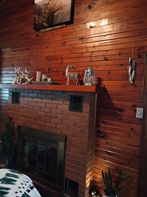Ein Kamin mit Ziegelverkleidung, ein Sims mit Dekorationen und eine Holzwand mit einem gerahmten Bild darüber.