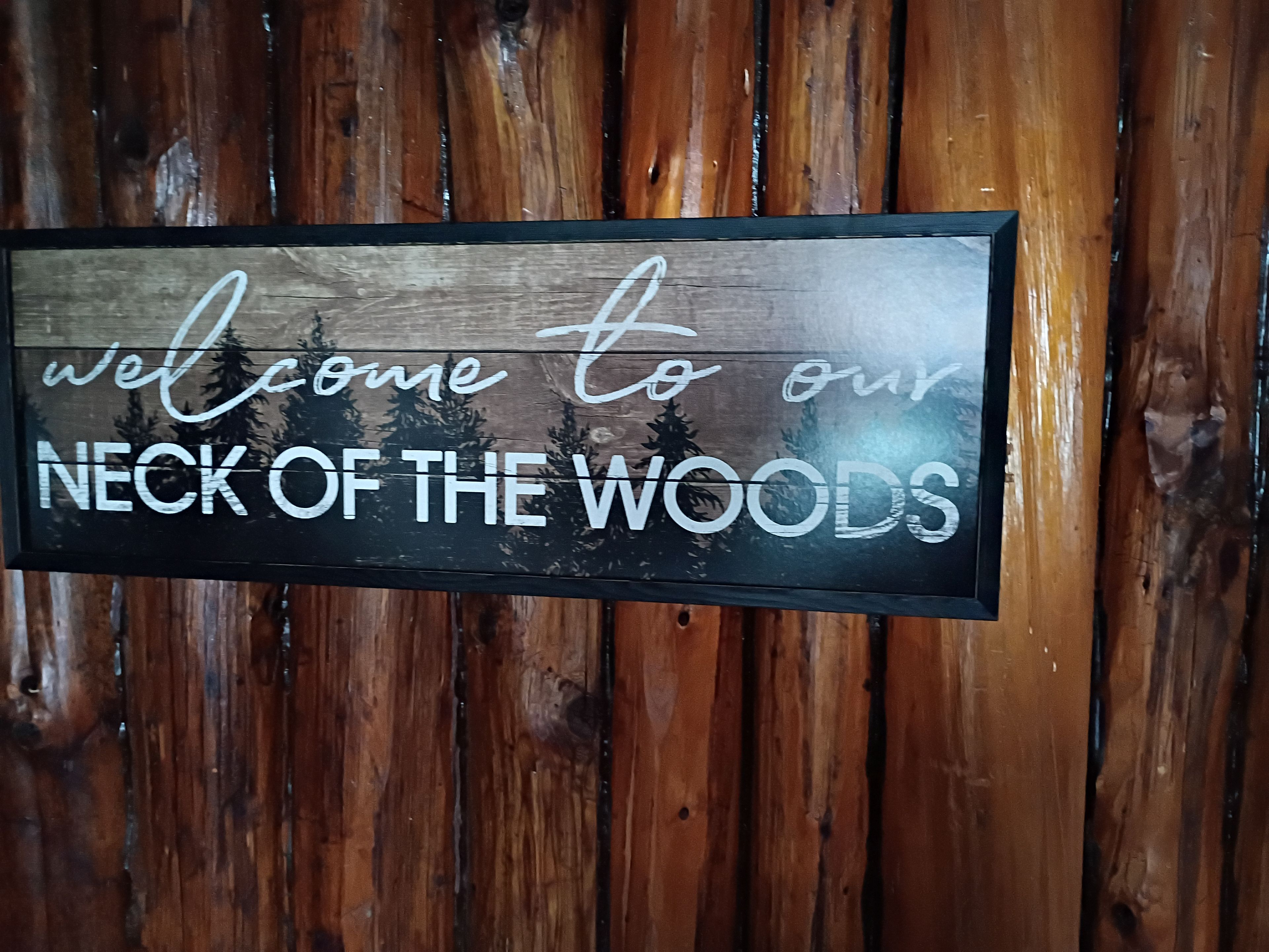 A welcome sign with the text 'welcome to our NECK OF THE WOODS' against a wooden background.