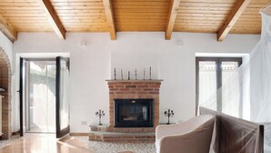 Een ruime kamer met een open haard, houten vloeren en een groot raam.