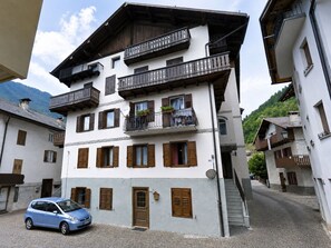 Ein mehrstöckiges Gebäude mit Balkonen, ein geparktes Auto davor und eine gepflasterte Straße.