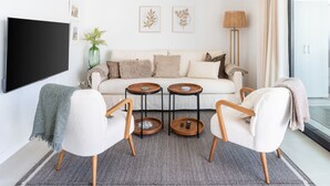 A modern living room with a sofa, two armchairs, a coffee table, a TV, and artwork on the wall. - Higuerón West Alicia | Modern Apartment with Garden & Pool View (Fuengirola)