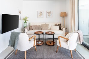 Una sala de estar moderna con un sofá, dos sillones, una mesa de centro, un televisor y obras de arte en la pared.