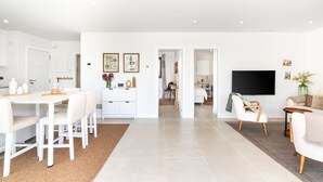 A modern, well-lit living space with a dining area, kitchen, and a TV mounted on the wall. - Higuerón West Alicia | Modern Apartment with Garden & Pool View (Fuengirola)