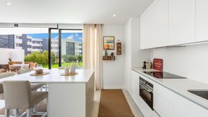 A modern kitchen with a large island, a dining area with a view, and a kitchenette. - Higuerón West Alicia | Modern Apartment with Garden & Pool View (Fuengirola)