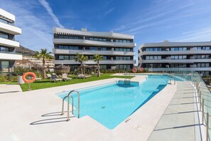 Ein modernes Hotel mit Pool, mehreren Balkonen und blauem Himmel.