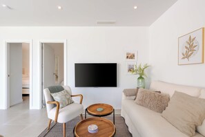 Ein modernes Wohnzimmer mit Flachbildfernseher, einer Couch, einem Sessel und einem Couchtisch.