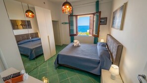 Ein Hotelzimmer mit Bett, Sitzecke, Fenster mit Meerblick und einer Pendelleuchte.