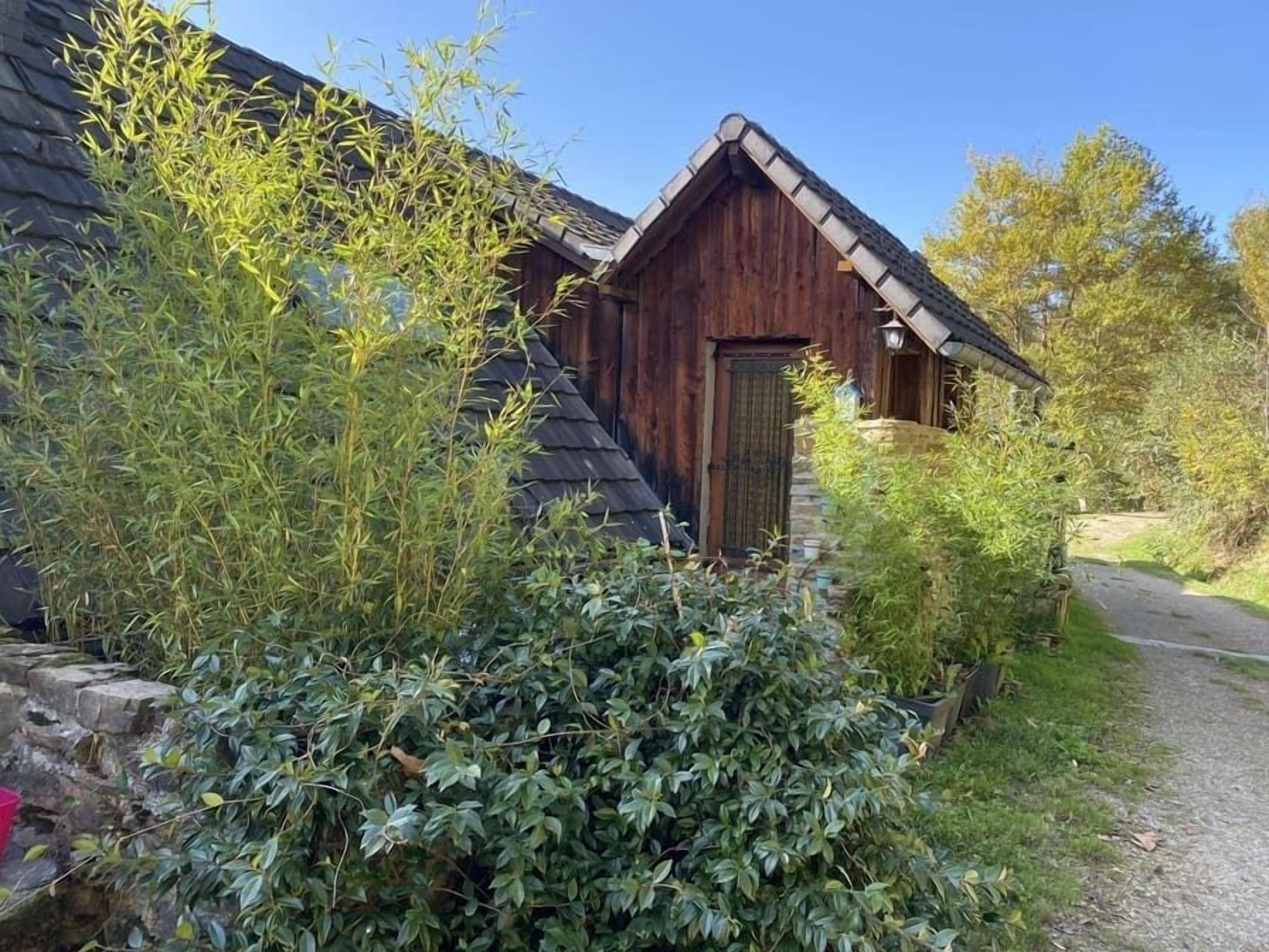 Un bâtiment rustique en bois, doté d’un toit en pente, entouré d’une végétation luxuriante et bordé d’un chemin de gravier.
