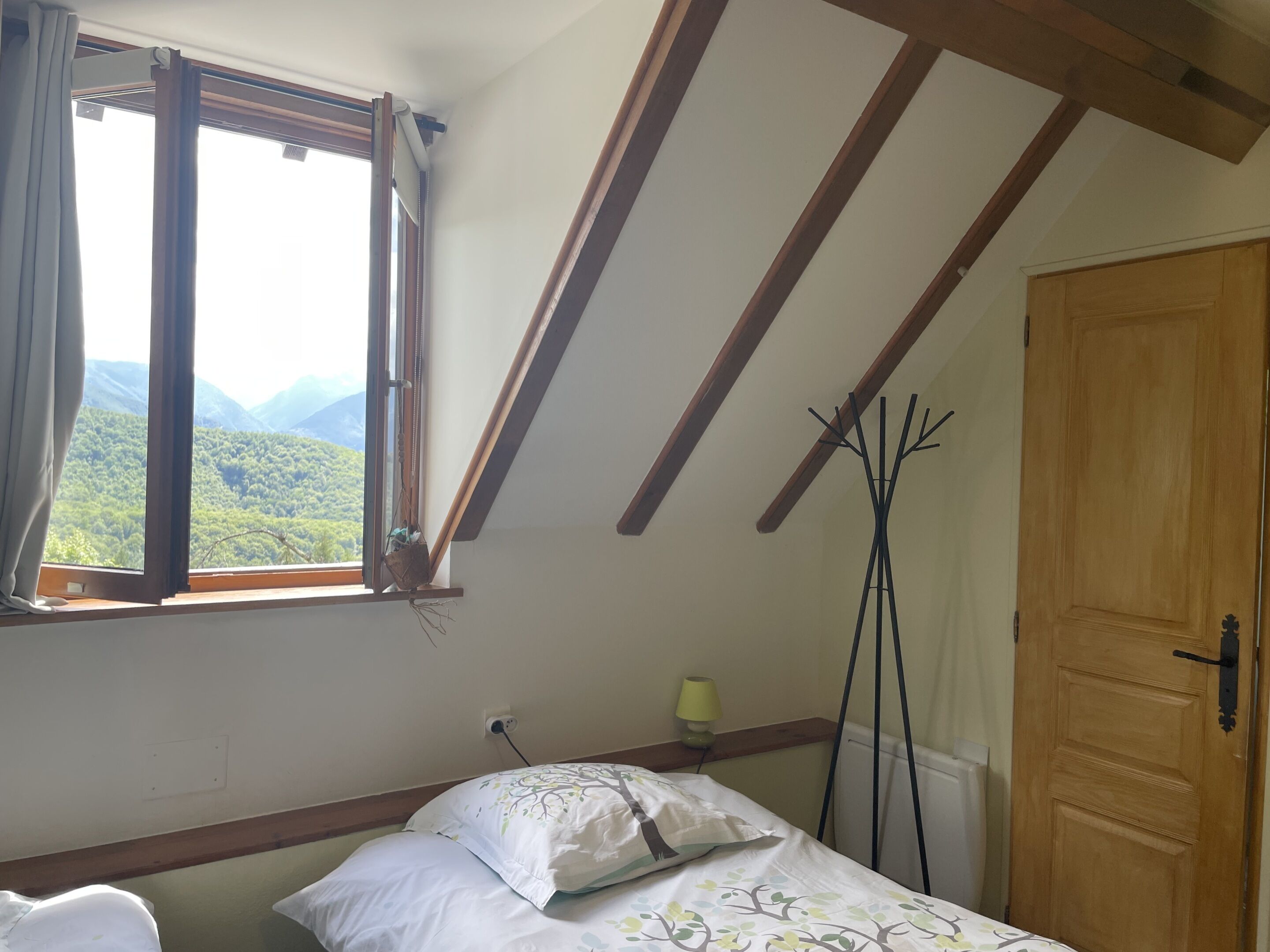 Une chambre avec une fenêtre, un lit, une lampe de chevet et une porte en bois.