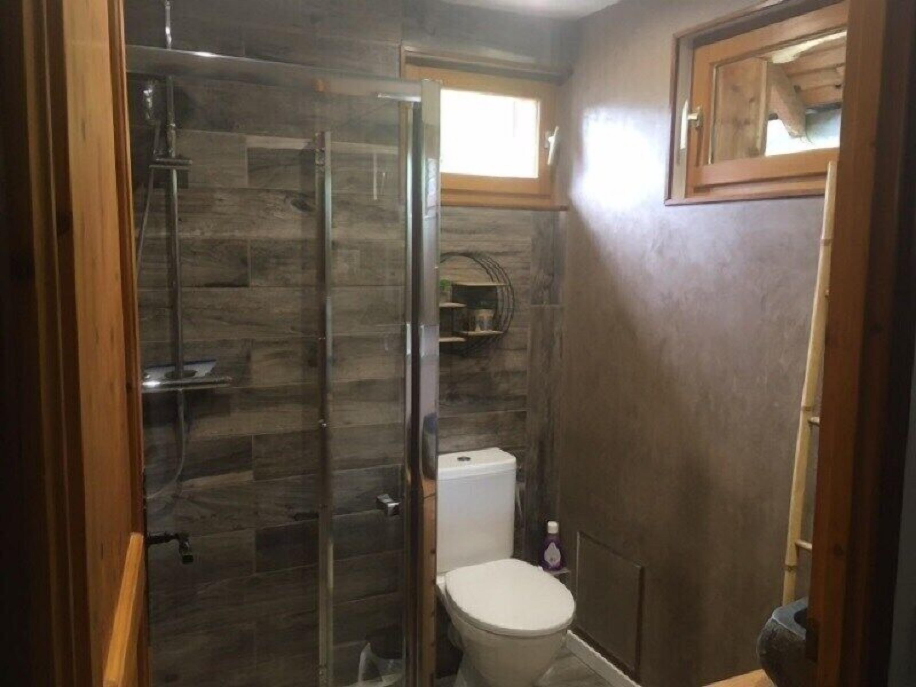 Un baño con cabina de ducha de vidrio, inodoro y una pequeña ventana.