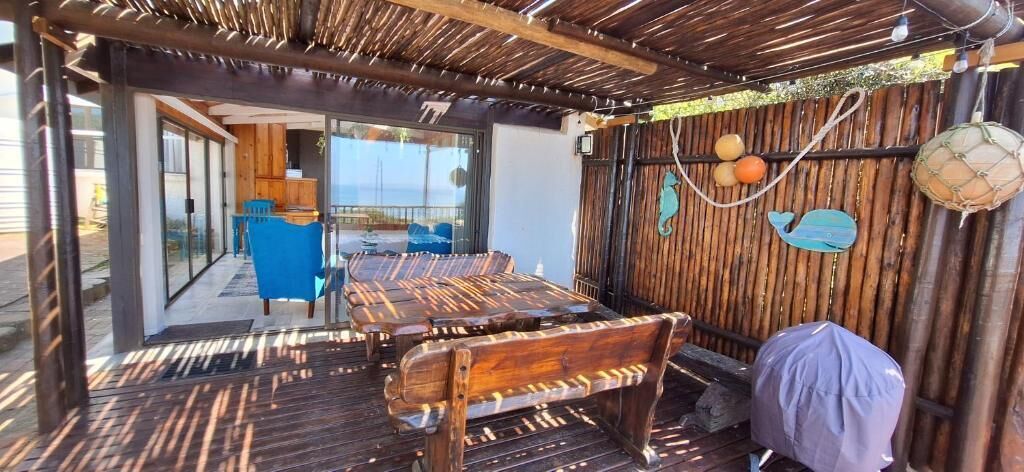 Un área de estar al aire libre cubierta, con bancos de madera, una mesa y sillas.