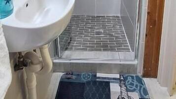 Un baño con lavamanos blanco, ducha con puerta de cristal y alfombra estampada en el suelo.