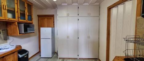 Una cocina con armarios de madera, microondas, refrigerador y un cubo de basura.