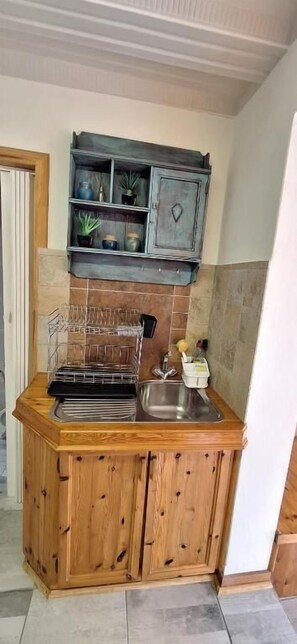 A compact kitchen with wooden cabinets, a built-in shelf with plants, a dish rack, and a sink. - Anca on C With Seaview (Klein Brak River)