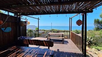 Una terraza de madera con un banco y una mesa, con vista al océano.