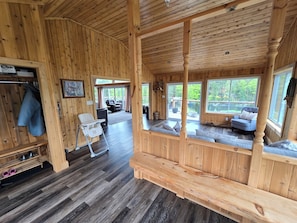 A wooden cabin interior with a dining area, a seating area with a view, and a small kitchenette.