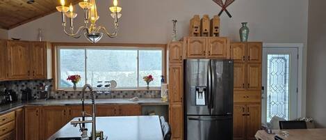 A kitchen with wooden cabinets, a stainless steel refrigerator, a chandelier, and a large window.
