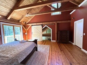 Een slaapkamer met een houten plafond, een bed, een dressoir en uitzicht op een balkon.