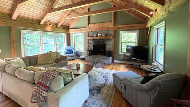 Un salón espacioso con chimenea, vigas de madera y ventanas grandes.