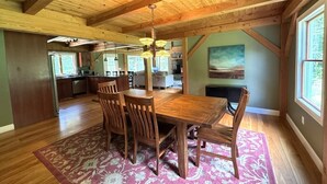 Un comedor amplio con una mesa y sillas de madera, un tapete estampado y vistas a la cocina y al salón.