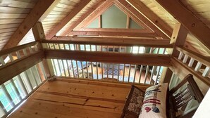 Una habitación de desván con techo inclinado, vigas de madera y vistas por la ventana.