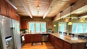 Una cocina con armarios de madera, un refrigerador de acero inoxidable, una isla de madera e iluminación colgante.