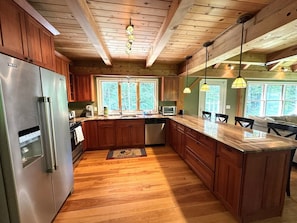 Een keuken met houten kasten, een roestvrijstalen koelkast, een houten eiland en hanglampen.
