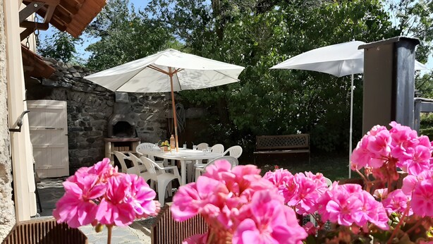 Eine Außenpatio mit Steinmauern, einem Steinofen, weißen Sonnenschirmen und rosa Blumen.