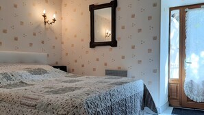 Ein Schlafzimmer mit einem Bett, einem Wandspiegel und einer Tür mit Spitzenvorhang.