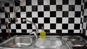 Une cuisine avec un dosseret à carreaux noirs et blancs, un évier en acier inoxydable et une bouteille jaune posée sur le comptoir.