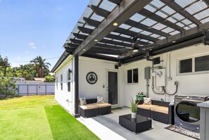 Eine überdachte Terrasse mit Sitzgelegenheiten, einer Waschmaschine und einer Wanduhr.