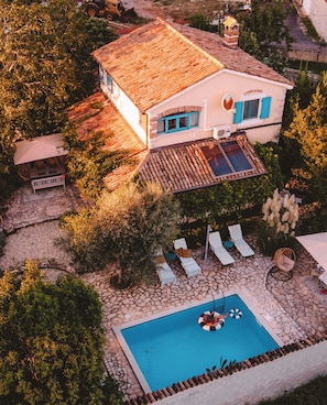 Ein Luftbild eines Hauses mit Ziegeldach, Schwimmbad und einem Garten mit Liegestühlen.
