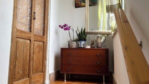 Un couloir avec une porte en bois, une commode en bois dotée de tiroirs, un miroir et une plante en pot.