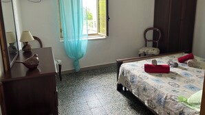 Une chambre à coucher comprenant un lit, une chaise, un bureau, une lampe, une fenêtre avec un rideau et un luminaire suspendu.