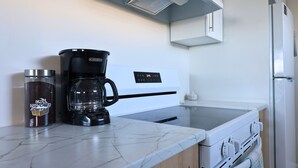 Een keuken met een koffiezetapparaat, een roestvrijstalen mok en een witte oven.