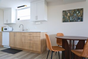 Una cocina moderna con armarios blancos, un microondas y un comedor con sillas de madera.