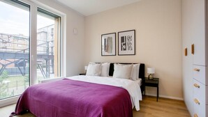 A bedroom with a large bed, a nightstand, a window with a view of buildings, and two framed pictures on the wall. - Blueground Holešovice, Family-friendly, nr Park (Prague)