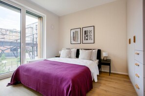 A bedroom with a large bed, a nightstand, a window with a view of buildings, and two framed pictures on the wall. - Blueground Holešovice, Family-friendly, nr Park (Prague)