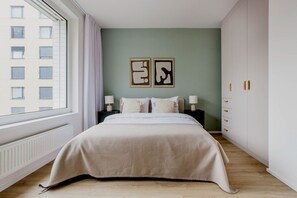 A bedroom with a large bed, two bedside tables with lamps, a window with curtains, and two framed artworks on the wall. - Blueground Apartments Prague 7 (Prague)