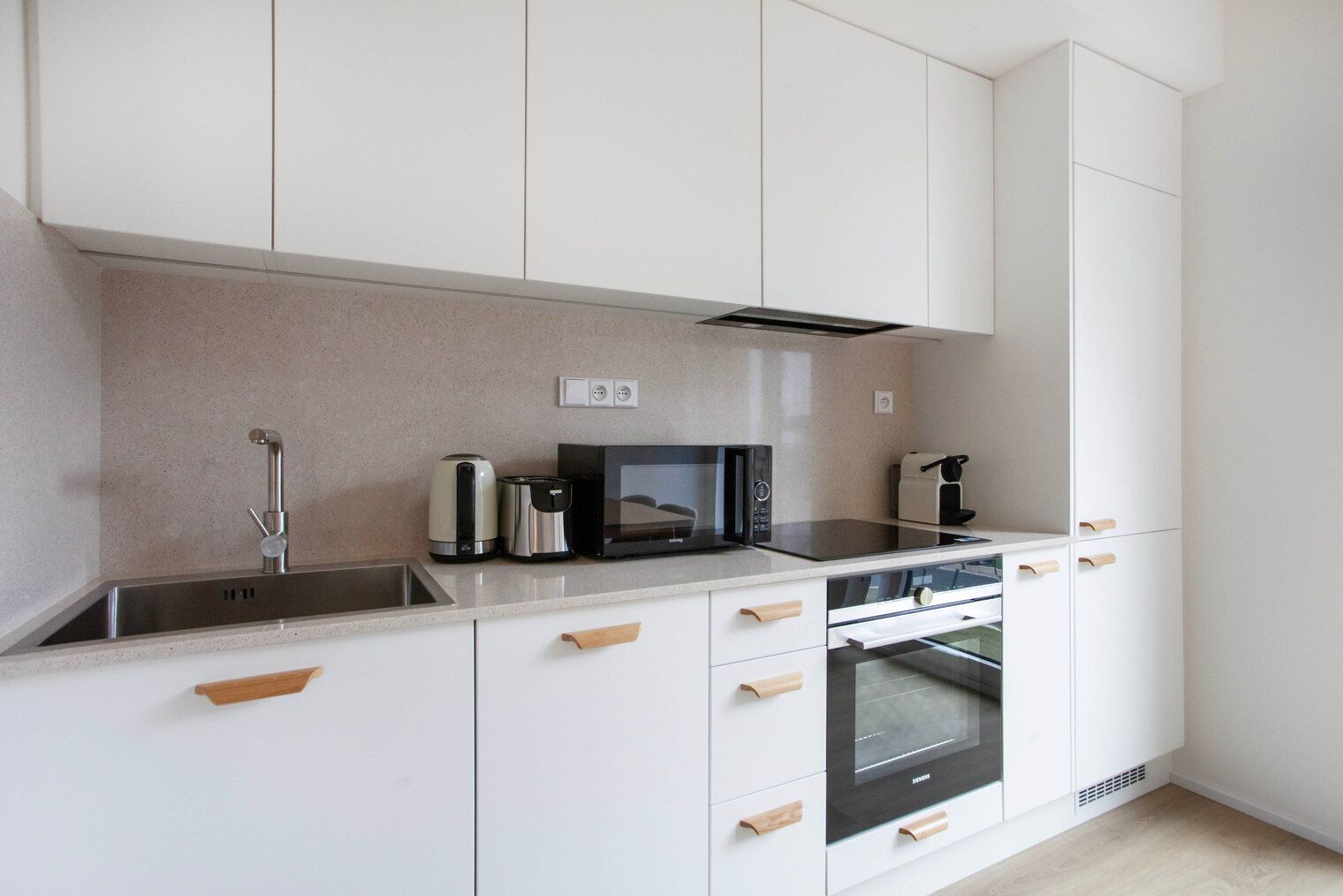 A modern kitchen with white cabinetry, a stainless steel sink, a microwave, a kettle, and a toaster.