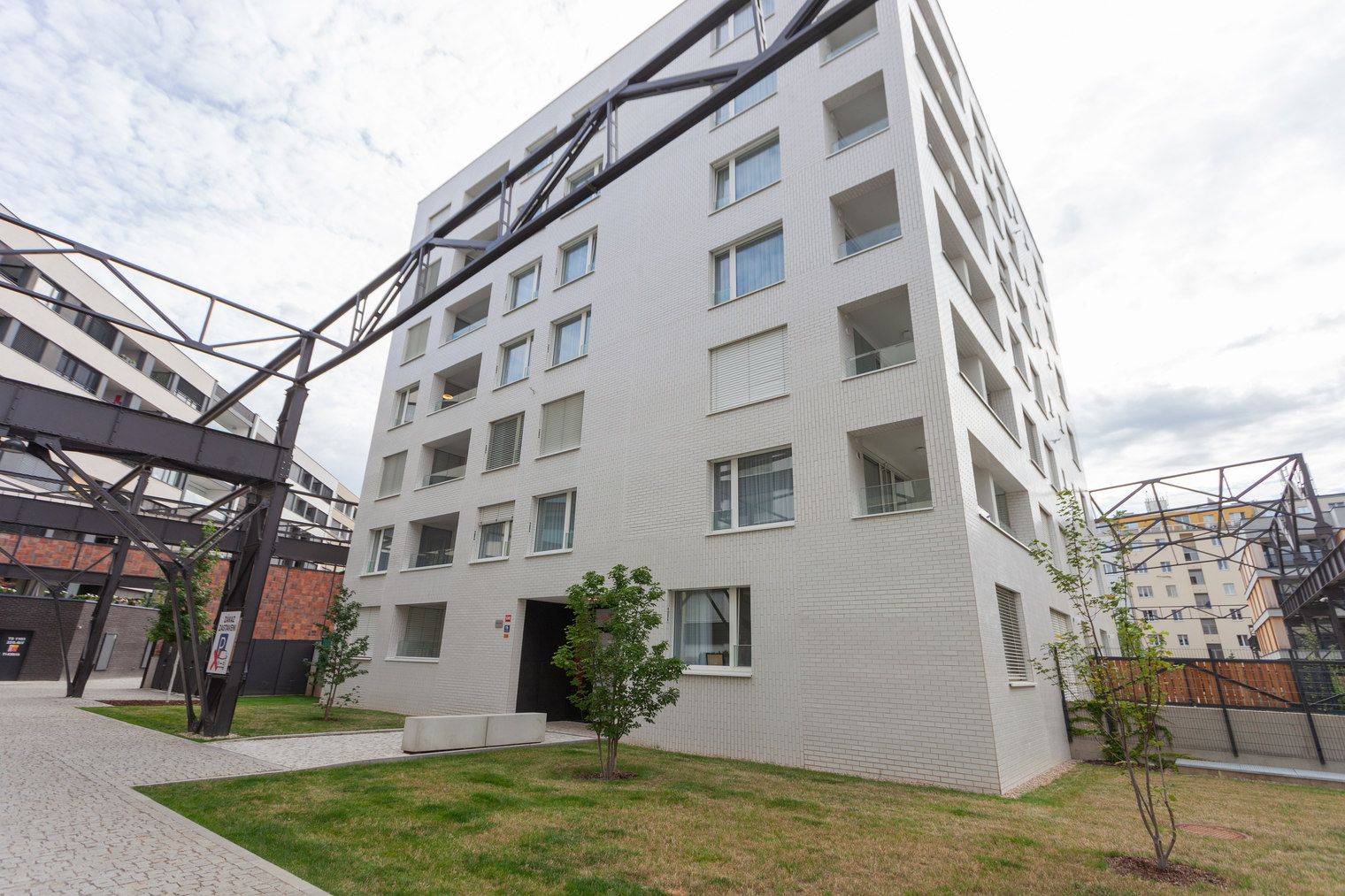 Un moderno edificio residencial de varios pisos con fachada blanca, múltiples balcones y un área de estacionamiento con un letrero que indica un costo por estacionamiento.
