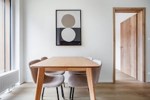 A modern dining area with a wooden table and chairs, a framed artwork on the wall, and a wooden door in the background. - Blueground Holešovice, Family-friendly, nr Park (Prague)