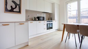 A modern kitchen with white cabinets, a microwave, and a coffee maker. There is a dining table with chairs and a window with a view of buildings. - Blueground Holešovice, Family-friendly, nr Park (Prague)