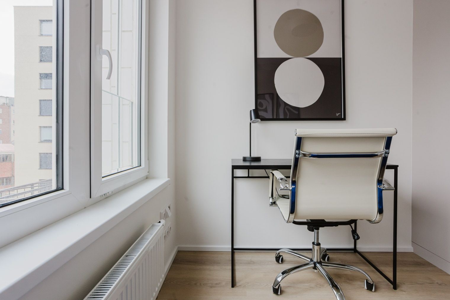 A modern office space with a window, a desk, a chair, and a wall-mounted artwork.