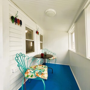 Eine überdachte Veranda mit zwei Stühlen und einem Tisch, weißes Holzverkleidung und ein blauer Boden.