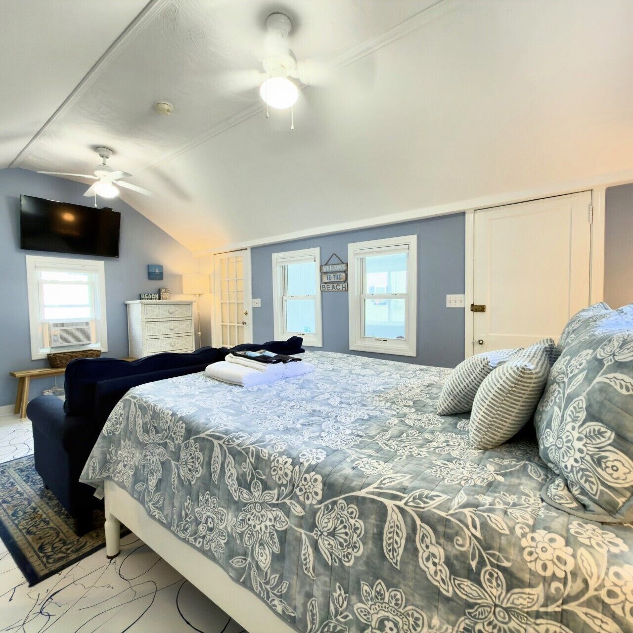 A bedroom with a bed, a ceiling fan, a TV, a dresser, and a window.