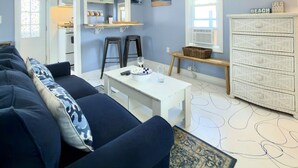 A living room with a sofa, a coffee table, a TV, and a kitchen in the background.