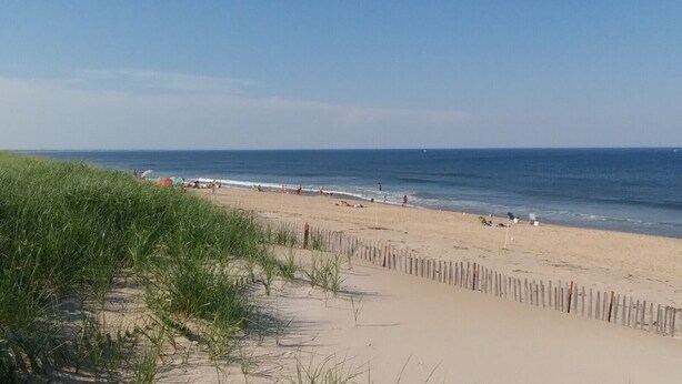 A beach with a wooden fence, sand, and the ocean.
