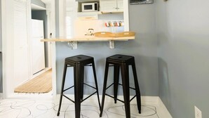 A kitchen with a microwave, a wooden shelf, and two black stools.