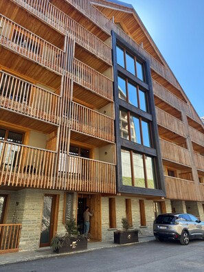Un edificio de varios pisos con balcones de madera, ventanas grandes y un coche estacionado frente a él.